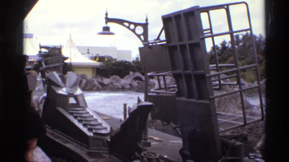 1974 Orlando home-movie frame from a ride boat, showing the vehicle, themed waterway rocks, lamp, and partial visitor figures.