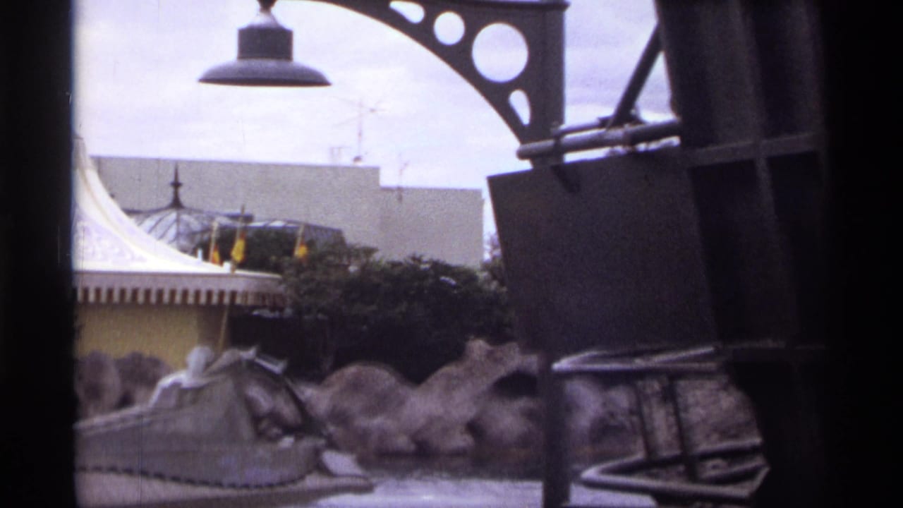 1974 Orlando 8mm frame showing a gray water-ride vehicle passing artificial rocks, partly blocked by dark foreground structure.