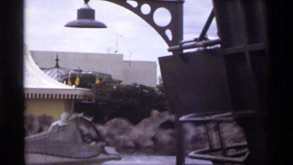 1974 Orlando 8mm frame showing a gray water-ride vehicle passing artificial rocks, partly blocked by dark foreground structure.