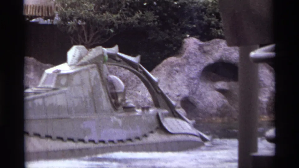 1974 Orlando 8mm frame showing the ride vehicle close to camera, with its curved canopy and rockwork partly hidden by a post.