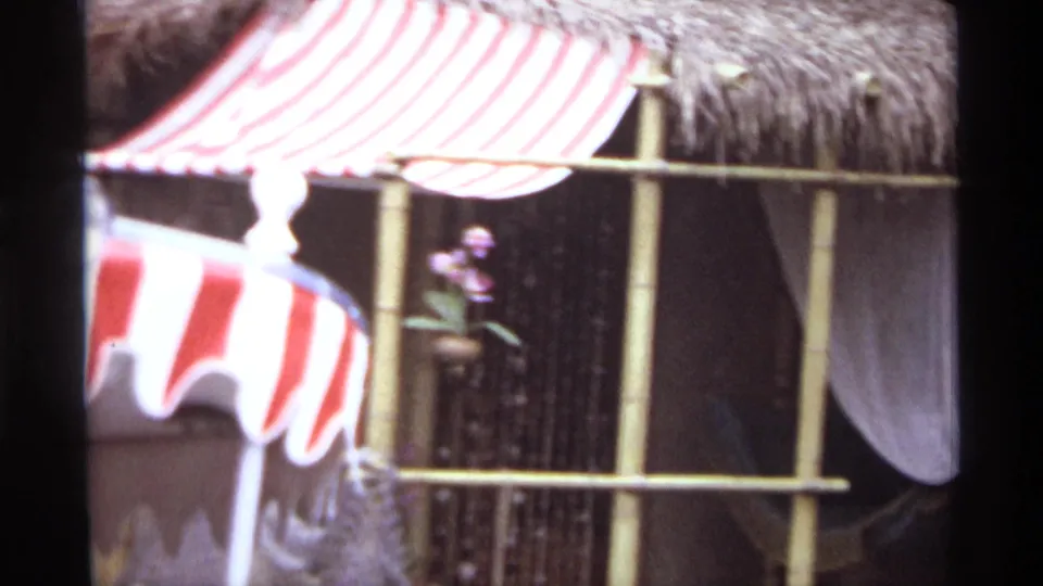 Soft 8mm frame from 1974 Orlando showing the red-and-white striped canopy of a boat near a thatched bamboo-style structure.