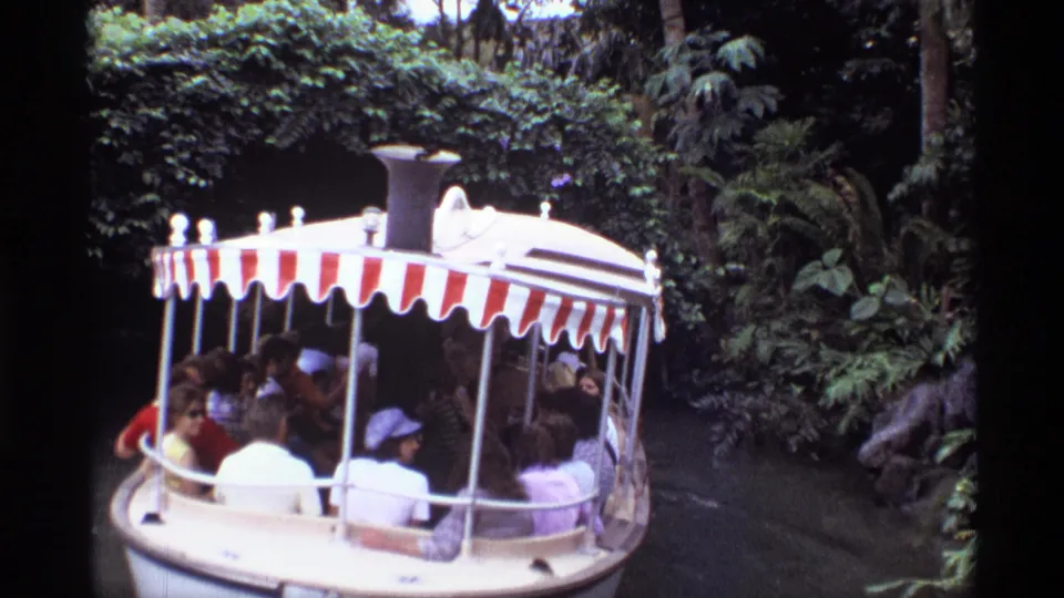 1974 Orlando home-movie frame showing a covered boat with seated passengers moving along a lush, narrow waterway.
