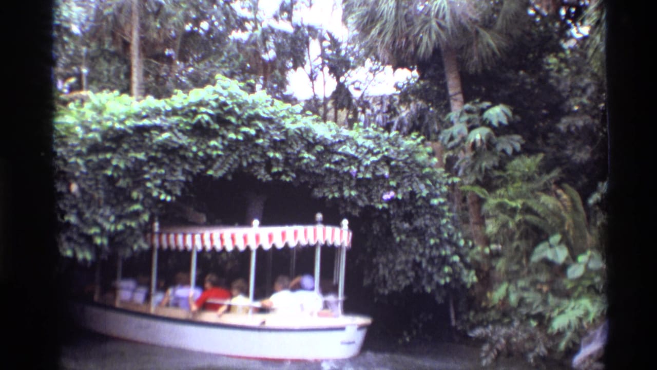 Small canopy boat entering a leafy tunnel beside dense tropical plants.