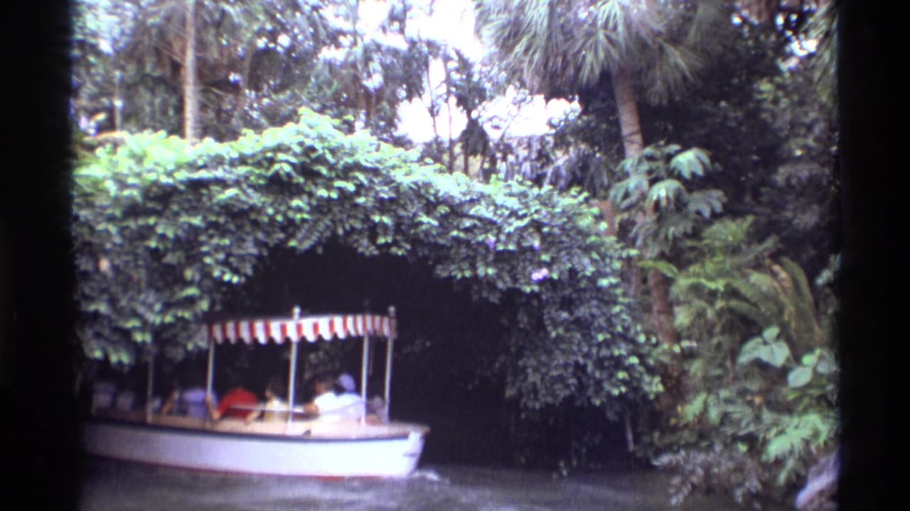 A 1974 Orlando attraction boat with passengers moves beneath dense vegetation toward a shaded tunnel opening.