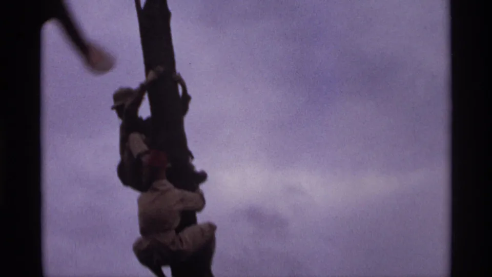 Close 1974 Orlando home-movie frame of figures gripping the upper part of a dark decorative pole against a pale overcast sky.