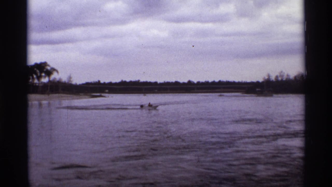1974 Orlando lagoon view with a distant rider on a small motorized craft crossing the water near a low shoreline.
