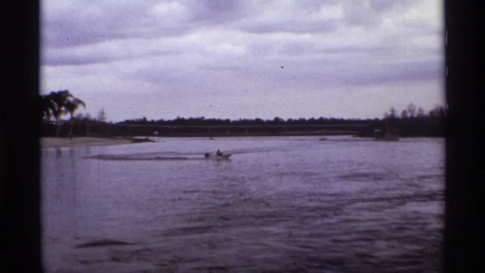 1974 Orlando lagoon view with a distant rider on a small motorized craft crossing the water near a low shoreline.