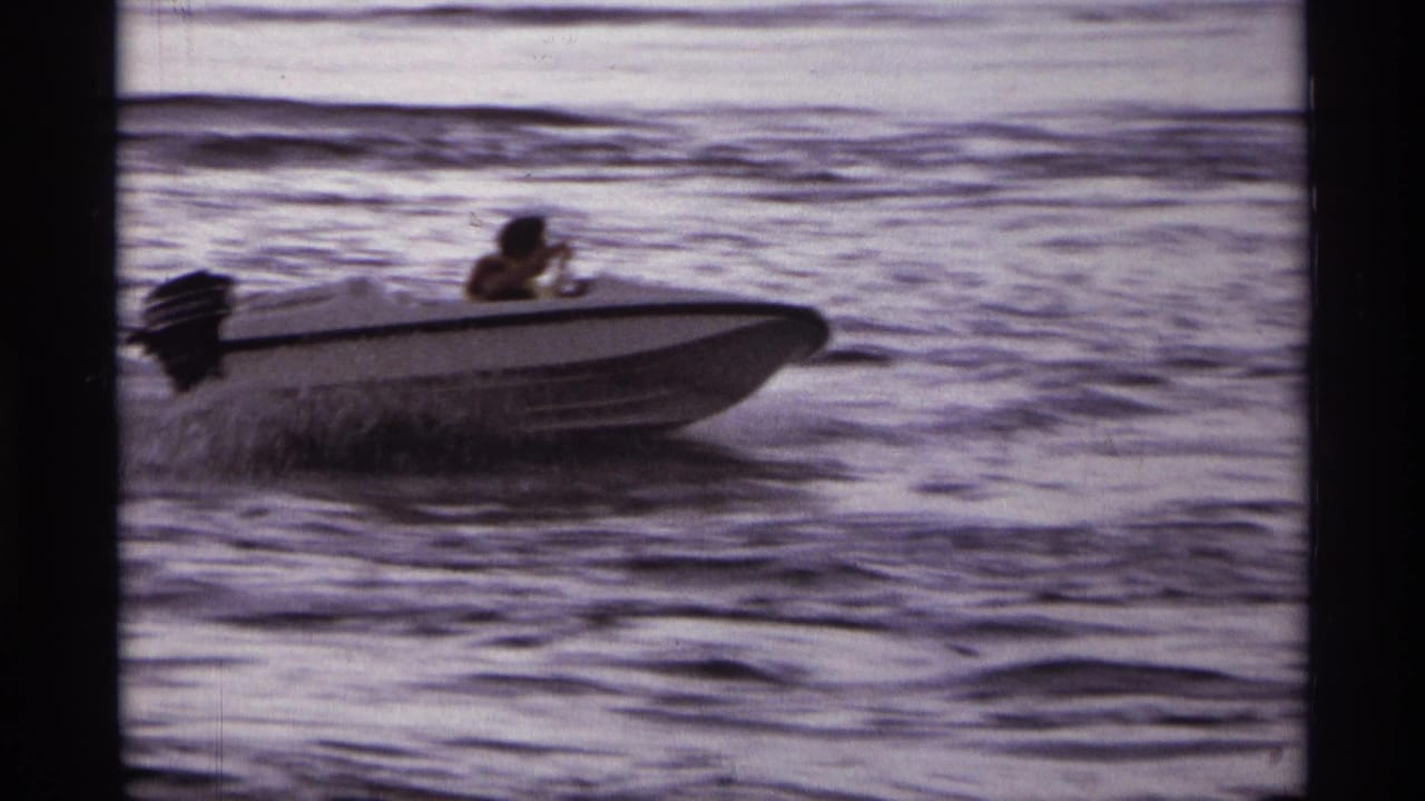 A man steers a white outboard speedboat across choppy lake water in 1974 Orlando-area home-movie footage.