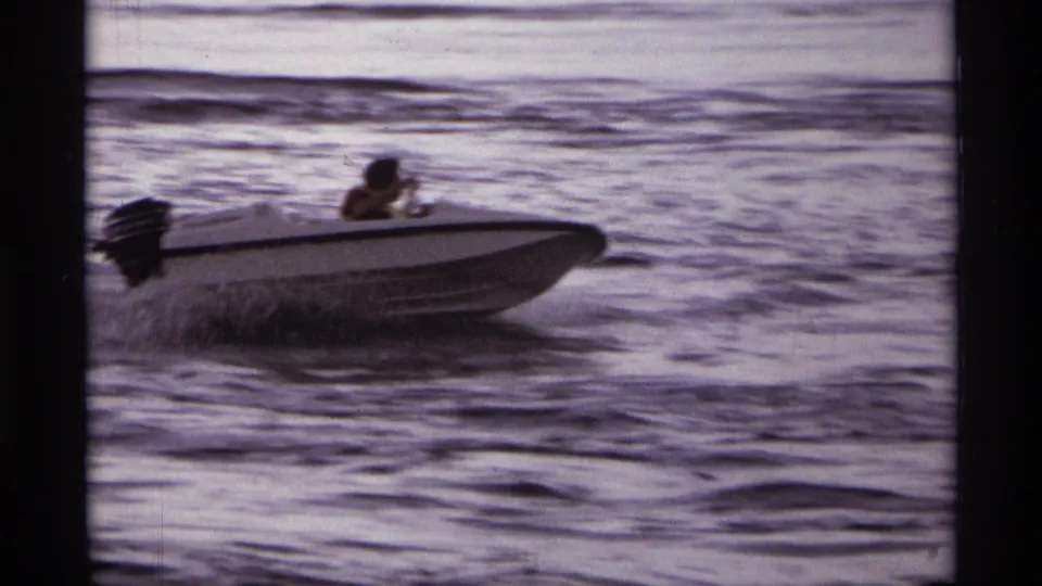 A man steers a white outboard speedboat across choppy lake water in 1974 Orlando-area home-movie footage.