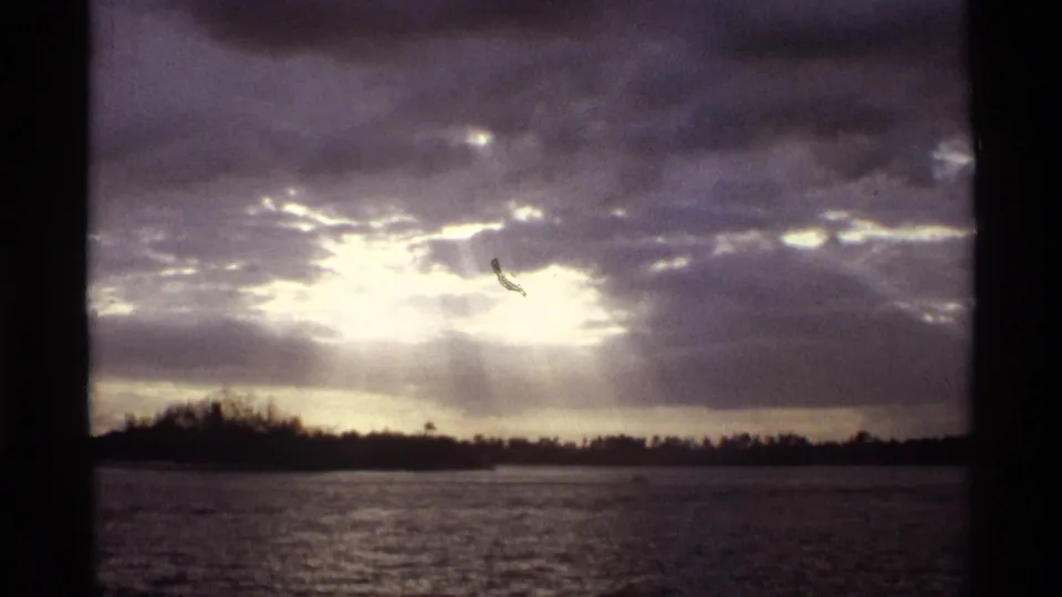 The final frame holds on a cloudy lake sunset, with bright light behind the clouds and a low shoreline in the distance.