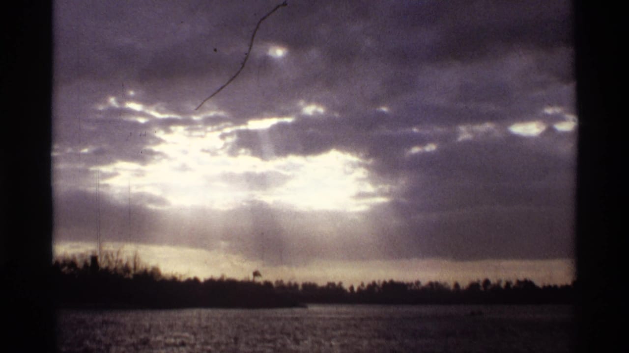 1974 Orlando-area 8mm frame with glowing cloud breaks, water below, and trees silhouetted along the horizon.