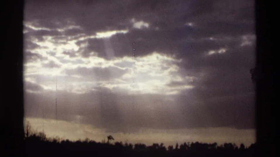 1974 Orlando-area 8mm frame emphasizing cloud texture, sun rays, water, and a silhouetted tree line.