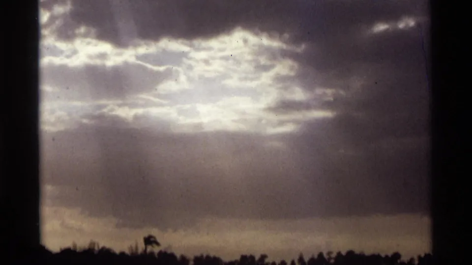 1974 Orlando-area 8mm frame showing luminous clouds, soft sun rays, water, and distant trees at the horizon.
