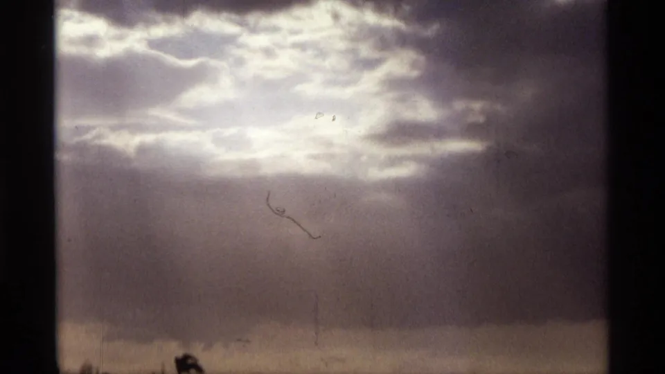 1974 Orlando 8mm frame showing bright sunlight diffused through layered clouds above a dark horizon line.