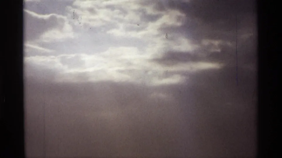 1974 Orlando 8mm frame with a luminous cloud opening and soft vertical shafts of light in an overcast sky.