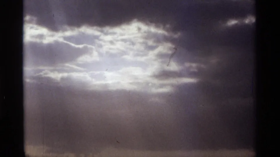 1974 Orlando 8mm frame showing a bright break in dark cloud cover with faint rays descending through haze.