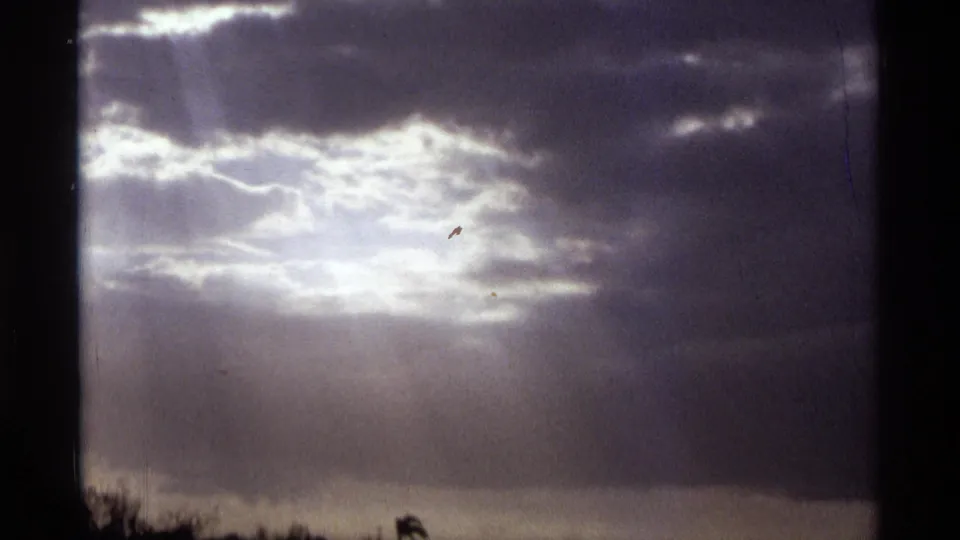 1974 Orlando-area 8mm frame showing storm clouds with bright sunlight breaking through above a dark shoreline silhouette.
