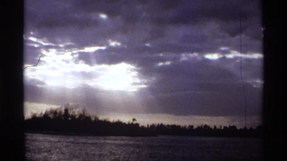 1974 Orlando-area 8mm frame showing bright cloud glare above rippled water and a silhouetted shoreline.
