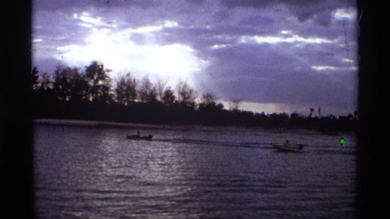 Two small motorboats cross a river below a cloudy sky and dark tree-lined shore.