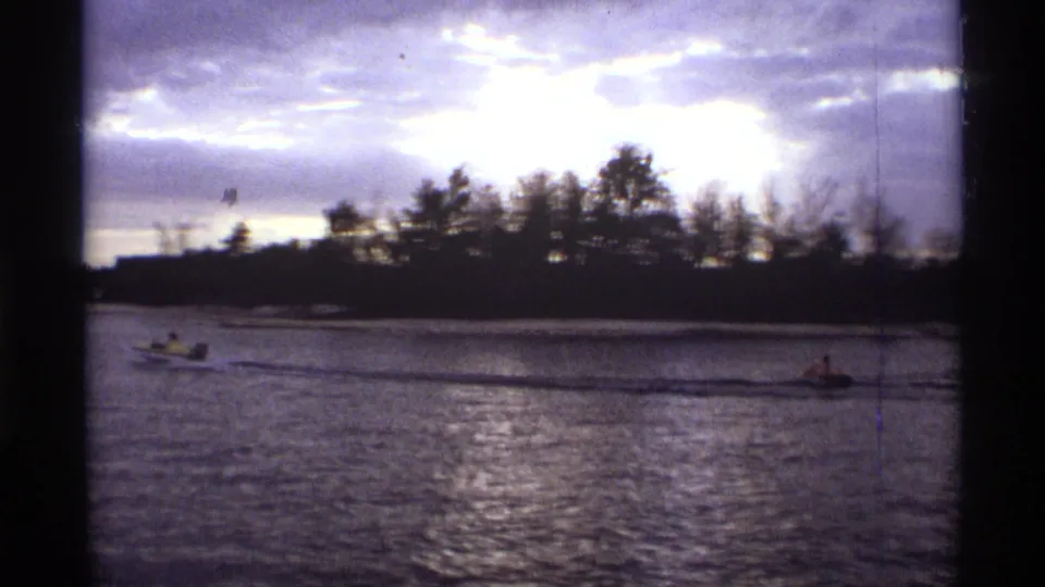 1974 Orlando 8mm frame showing a small boat on rippled water with a dark shoreline and overcast sky.