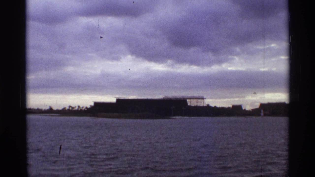 Wide view across water toward a low dark building beneath heavy clouds.