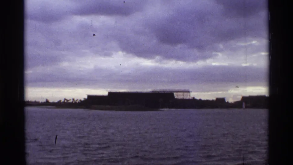 1974 Orlando 8mm frame showing rippled water, a distant low modern building, and a purple-gray overcast sky.