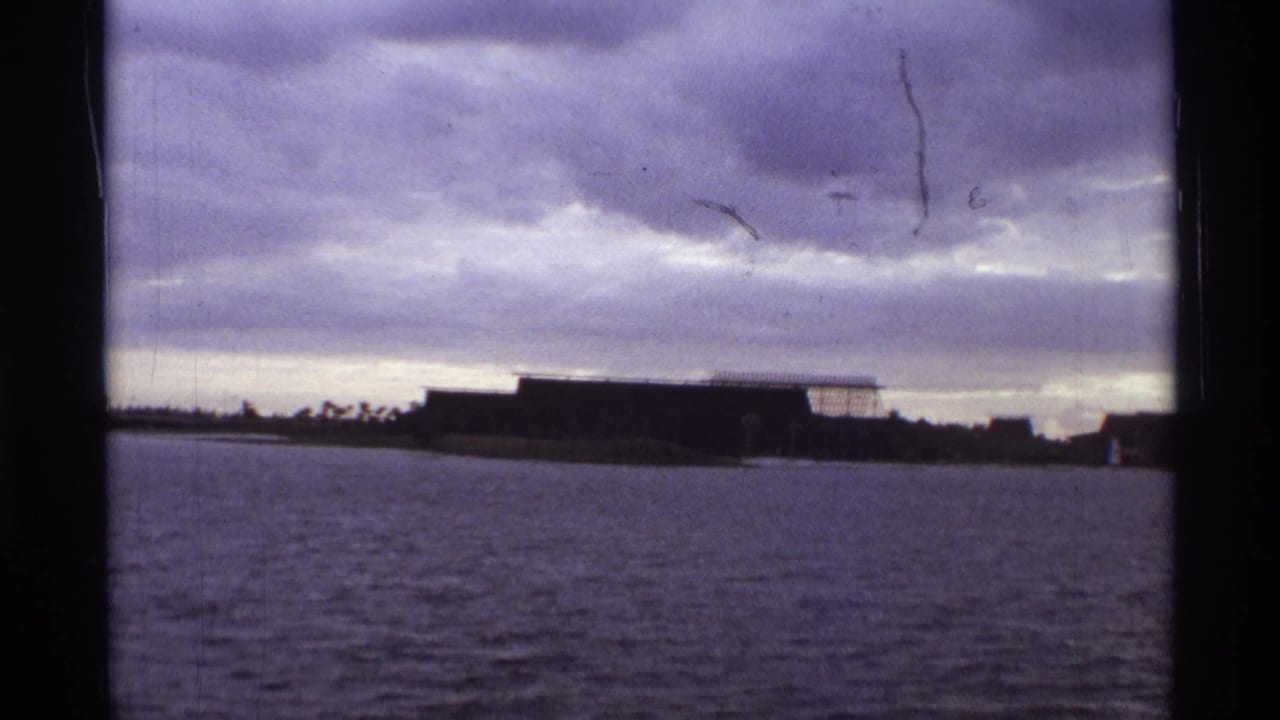 Distant low building across water with dark clouds filling the sky.