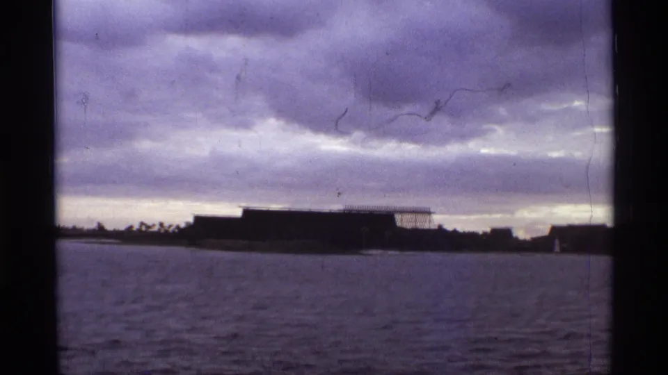 1974 Orlando frame showing a low waterside structure, cloudy horizon, rippled water, and visible film scratches.