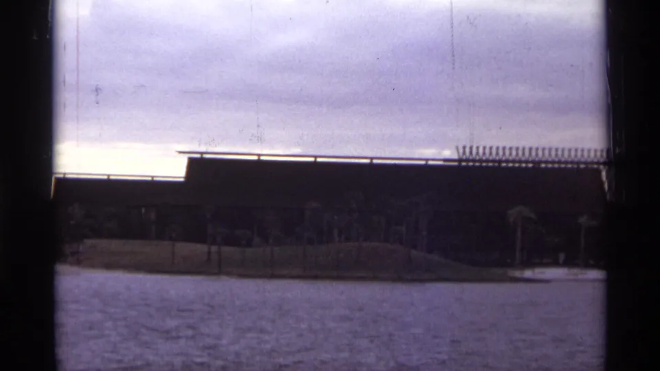 1974 Orlando home-movie frame with the brown building closer, palm trees along the bank and water in front.