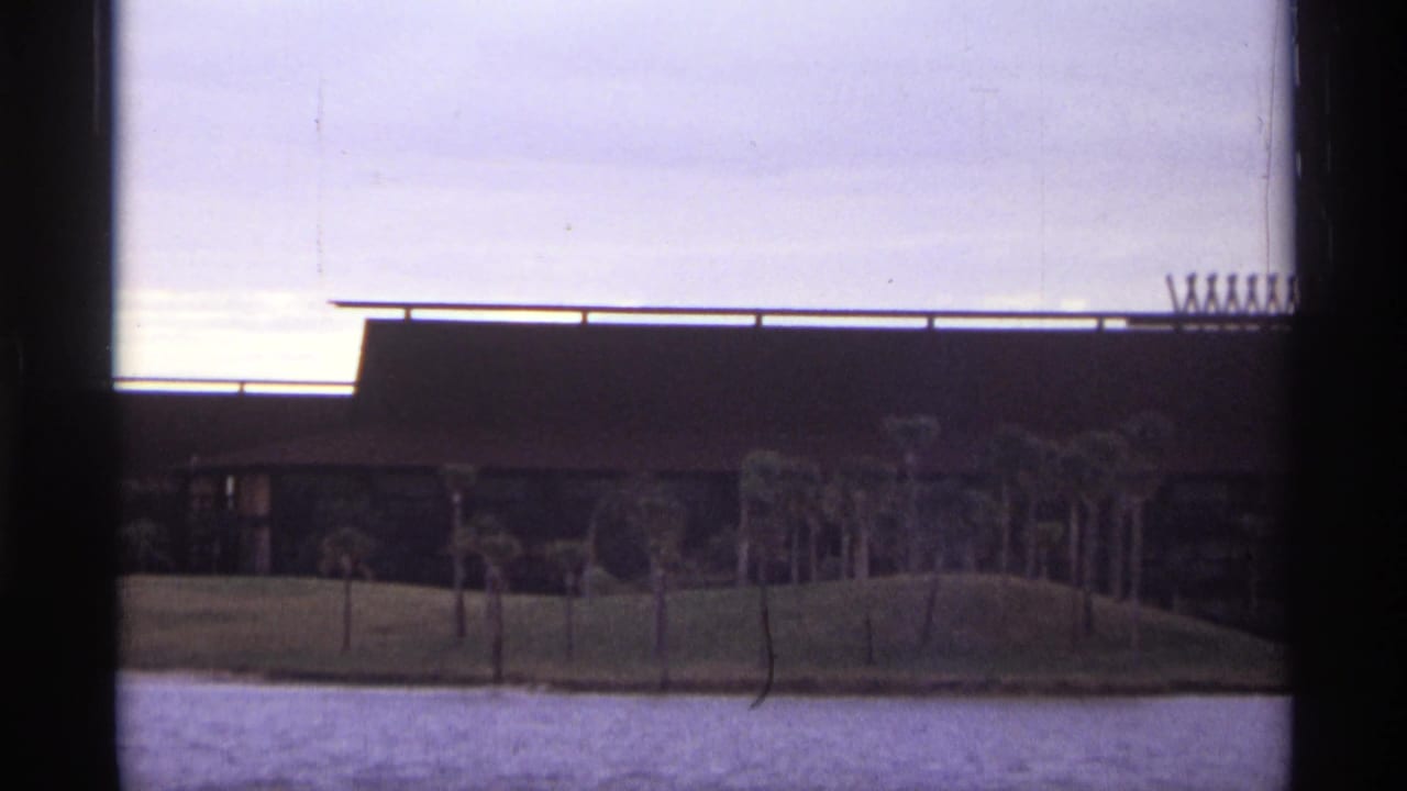 Long low building with palms on a shore across rippled water.