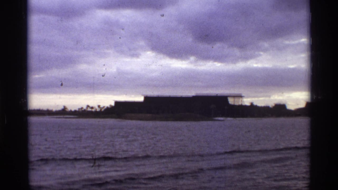 1974 Orlando-area view of a low waterfront structure on an island, seen through 8mm frame edges under a purple-gray sky.