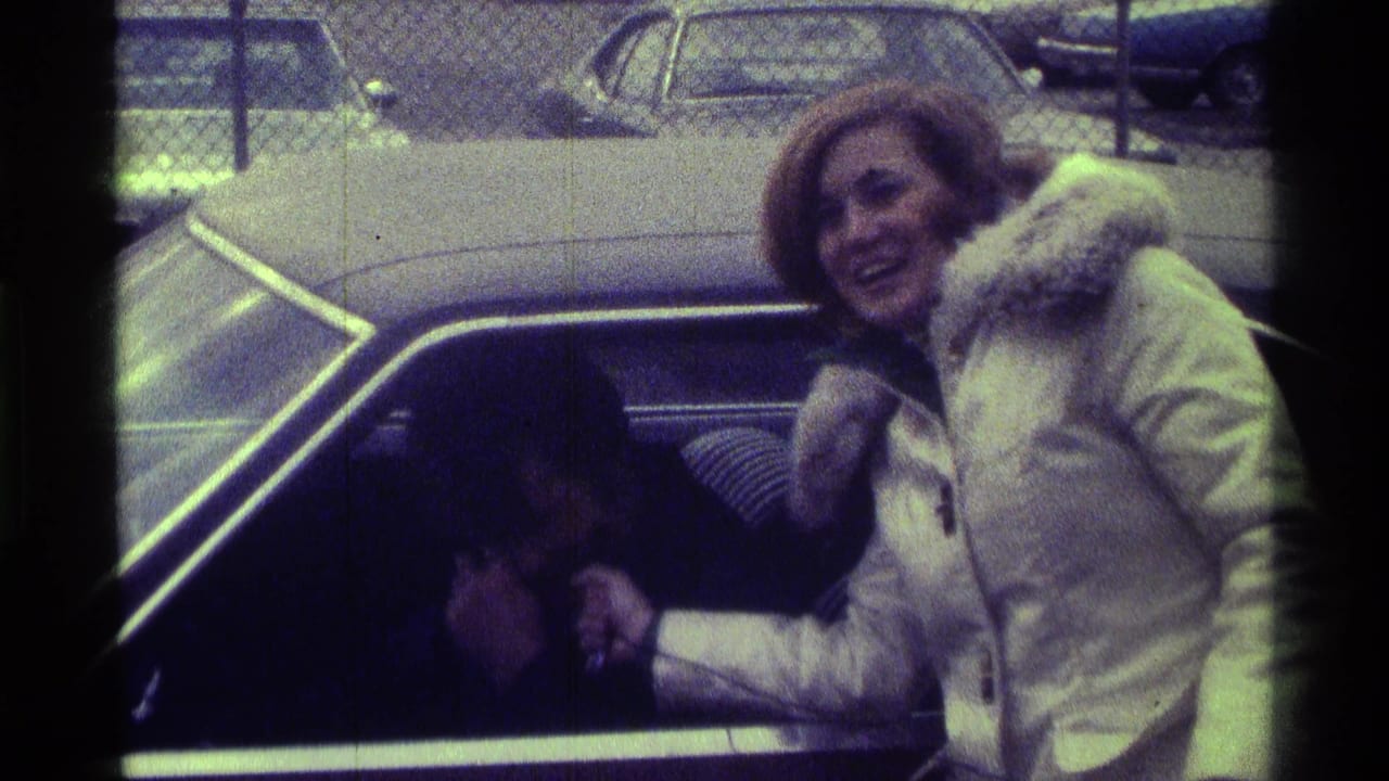 In 1976 Kentucky home-movie footage, a woman in a white winter coat laughs while leaning toward someone inside a vintage car.