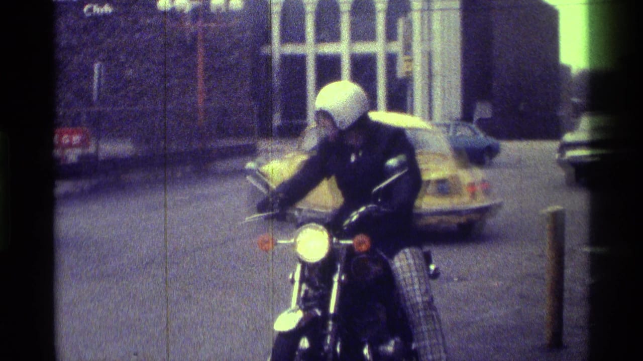 Helmeted motorcyclist on a street with a yellow Volkswagen Beetle behind him.