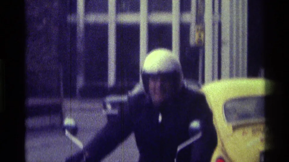 A closer, blurred 8mm frame shows the helmeted rider leaning near the motorcycle handlebars, with the yellow Beetle behind him.