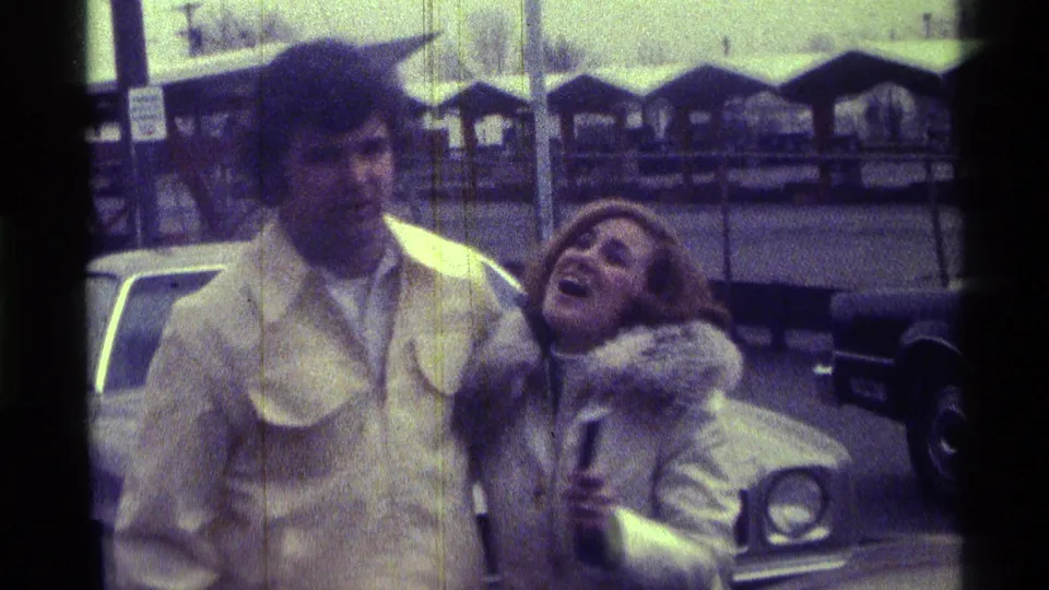 A woman in a fur-trimmed light coat laughs while holding a microphone beside a man in a beige jacket during the Kentucky street interaction.