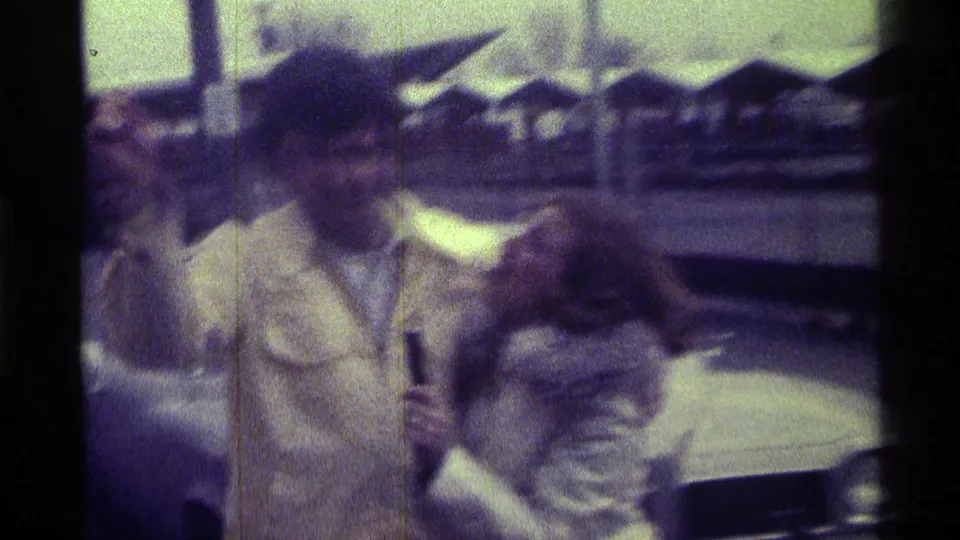The woman appears to playfully interview the man with a small handheld object while they stand near a car in the 1976 Kentucky footage.