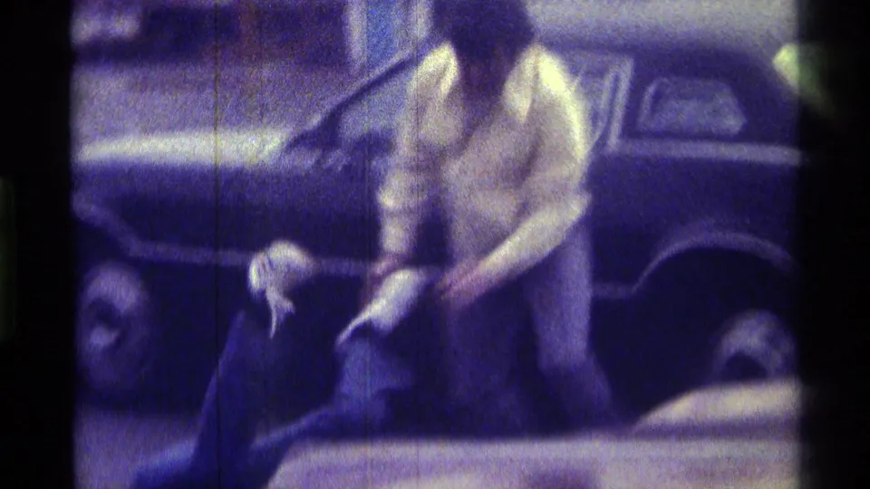 A woman in a fur-collared coat stands by a dark car in the Kentucky 1976 footage while another person is partly visible lower in frame.