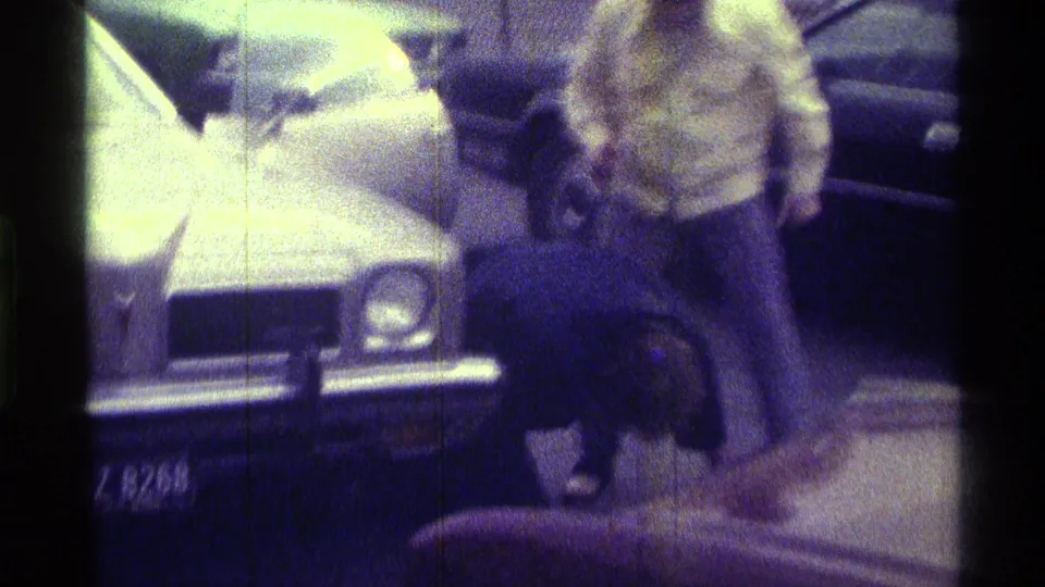 In a grainy parking-lot view, the man stands close to another person near two parked cars in the Kentucky 1976 clip.