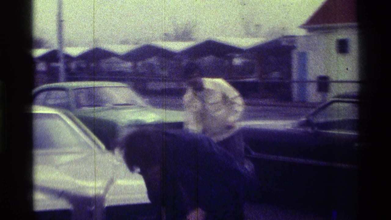 Two adults stand near parked cars beside a covered roadside structure.