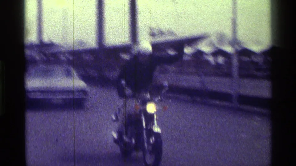 The helmeted rider draws closer on a residential or small-town Kentucky street, with cars parked along both sides.
