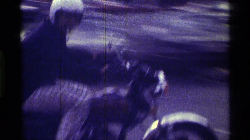 A blurred close pass shows the motorcycle moving by the camera, with the rider and front wheel partly visible in 8mm grain.