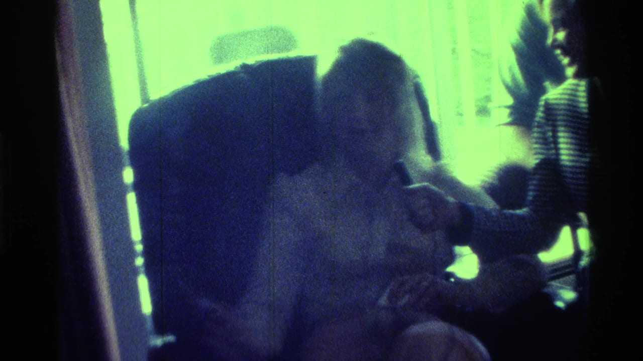 1976 Kentucky home-movie frame of a seated person in profile as another person holds a microphone near them beside a bright window.