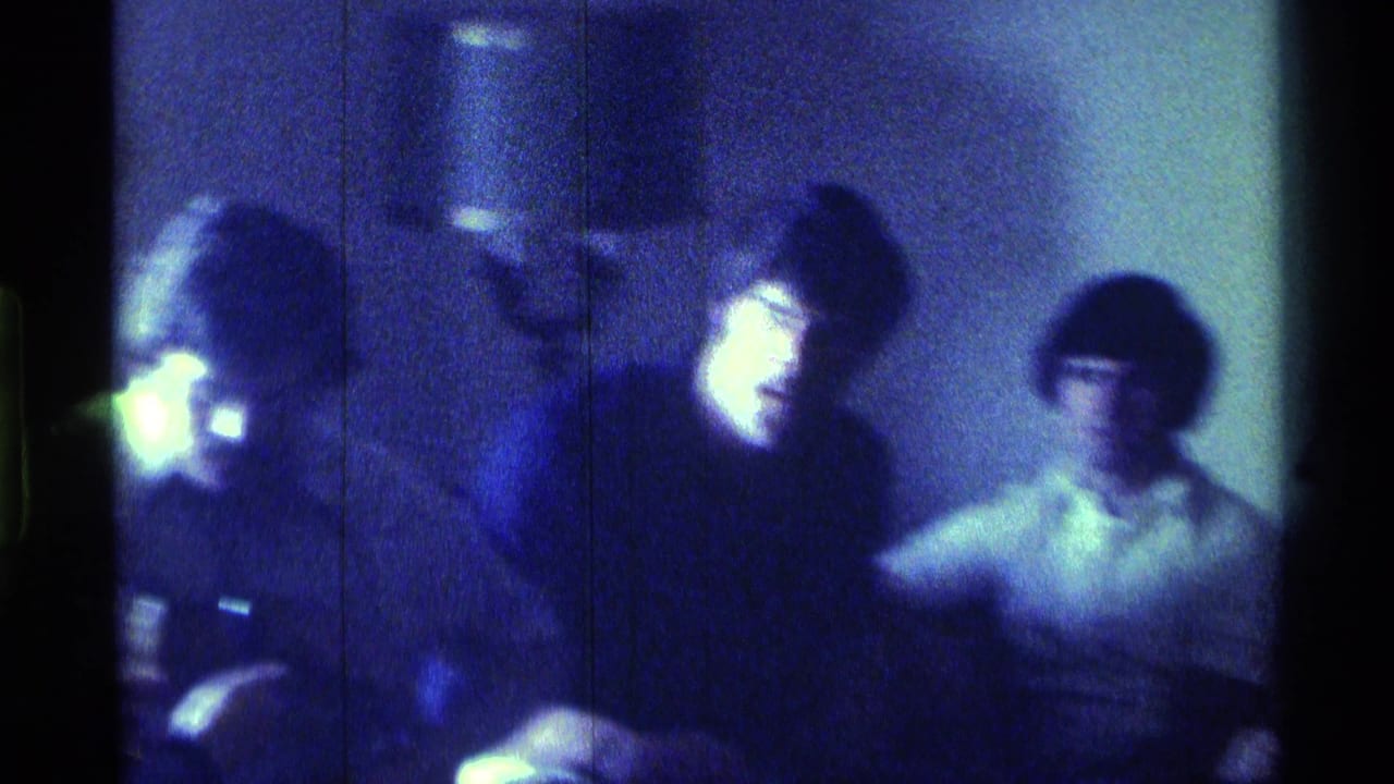 Dim low-light frame of several seated young men in a private room.