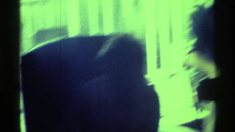 Heavily backlit home-movie frame with blurred figures near a bright window or curtain inside a private room.