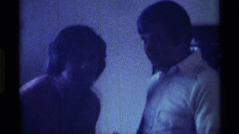 1976 Kentucky 8mm frame showing two partygoers in a dark interior, one leaning forward and one turned in profile.