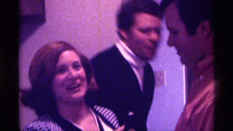 A woman in a checkered jacket smiles while standing near two men in a 1976 Kentucky private interior.