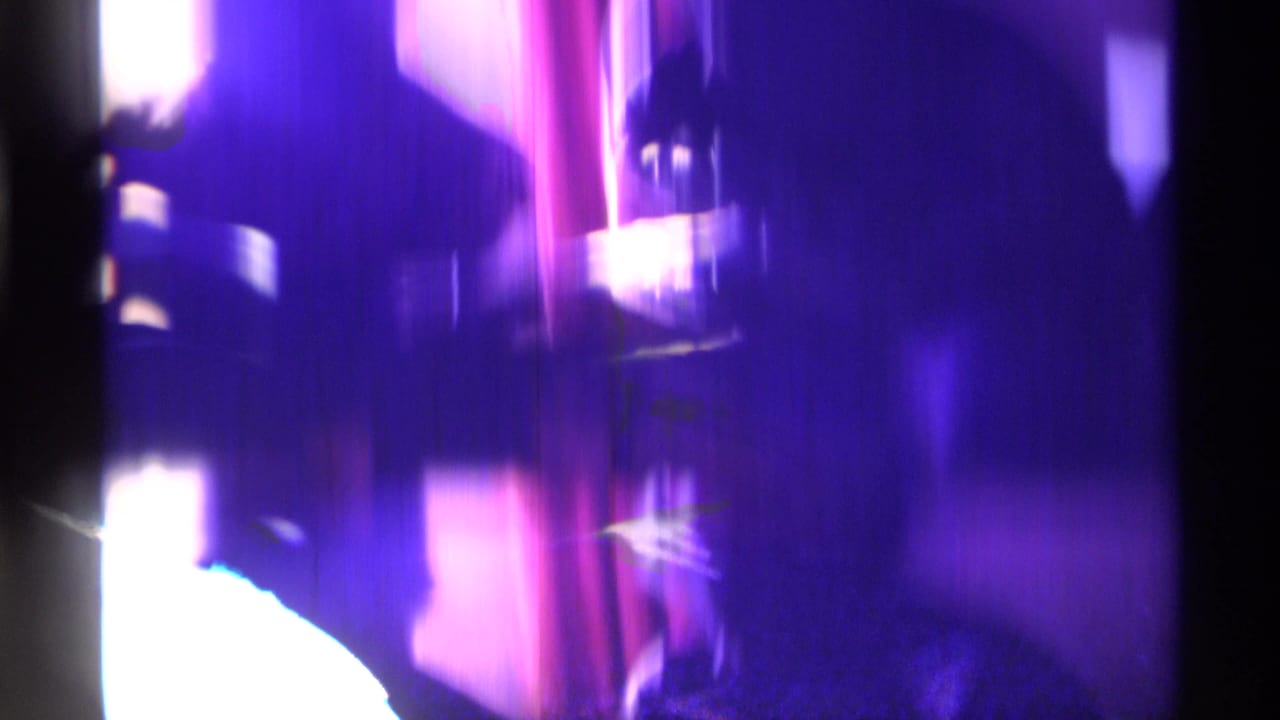 Purple-tinted, blurred home-movie frame with dark interior shapes and overexposed light areas.