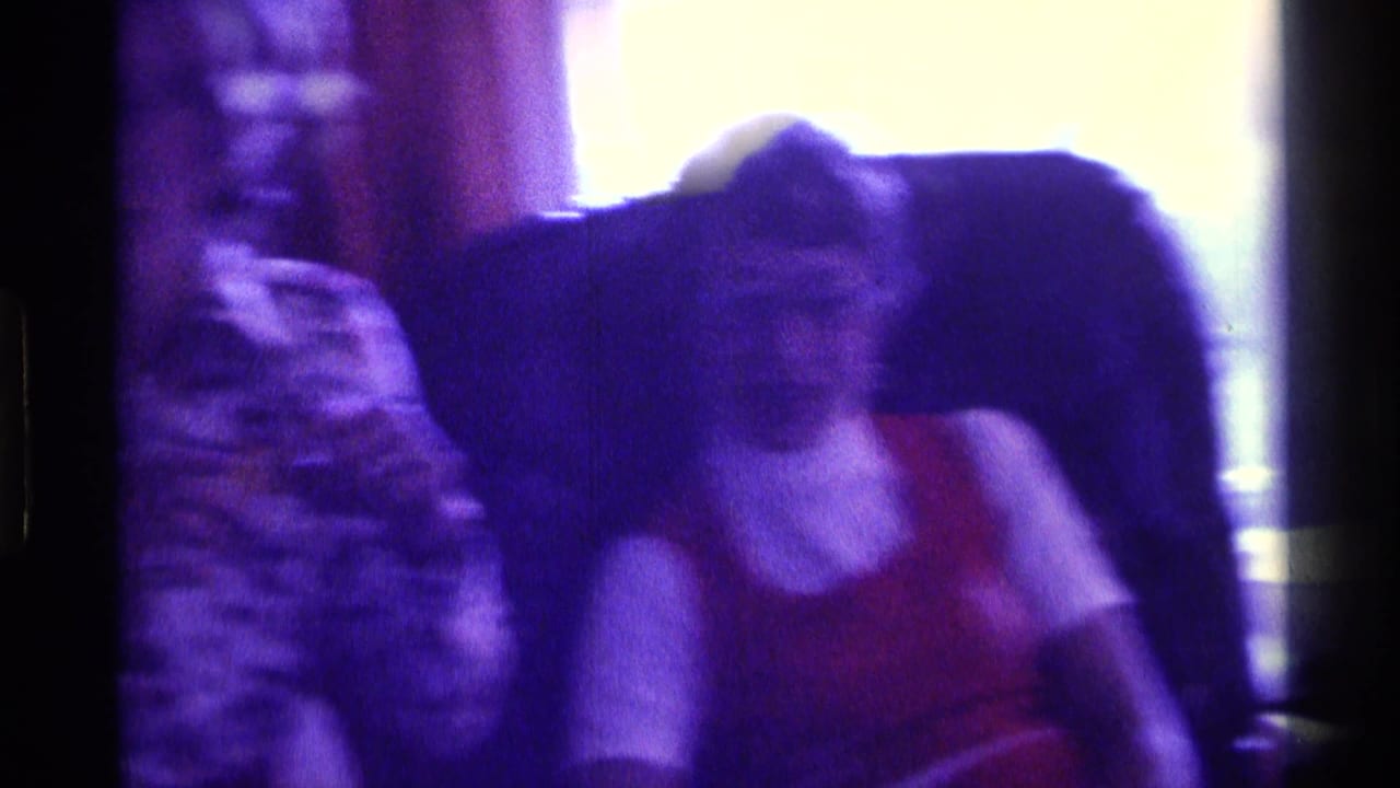 Purple-tinted 1976 Kentucky 8mm frame of adults seated together in a private interior, partly blurred by low light and motion.