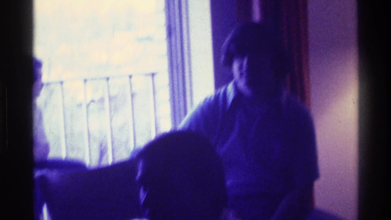 A man sits by a bright window in a purple-tinted Kentucky home-movie frame, with another person partially visible in front.