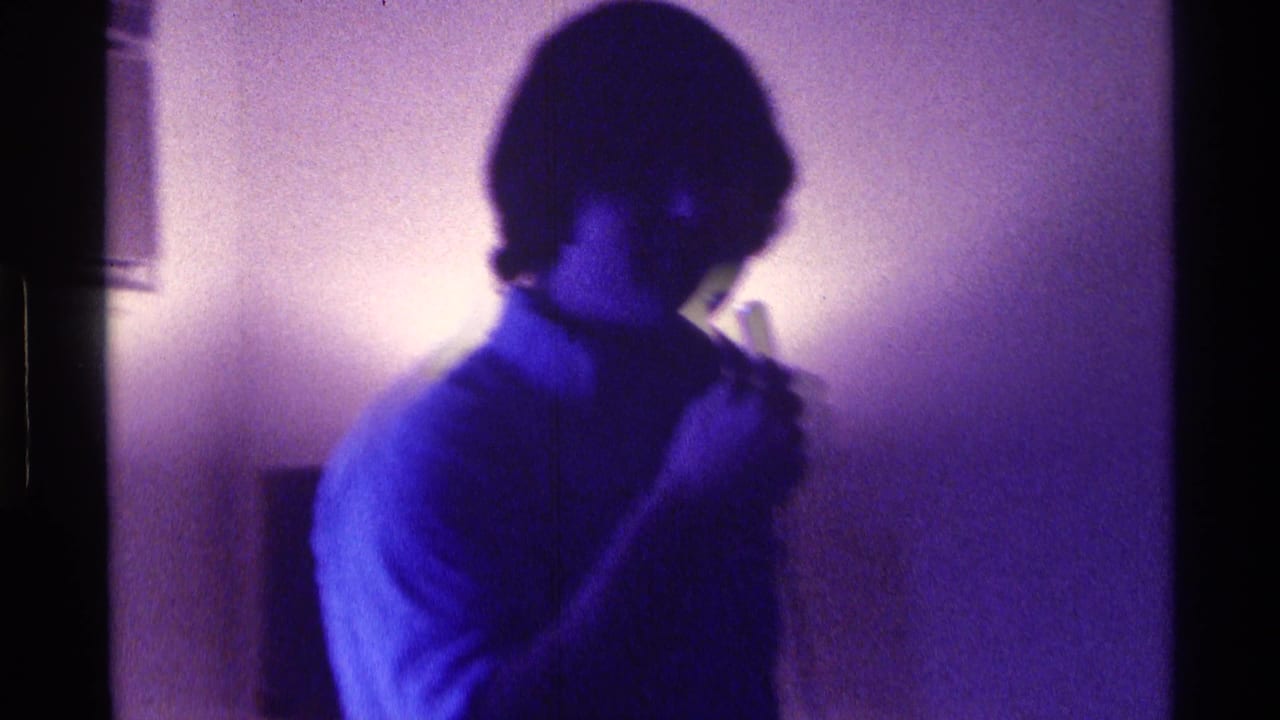 Young man at a 1976 Kentucky private gathering holds a microphone near his mouth under intense blue-purple light.